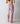 A person shown from the back wearing loose pink pajama pants with thin white vertical stripes and an elastic waistband, against a plain light gray studio background.